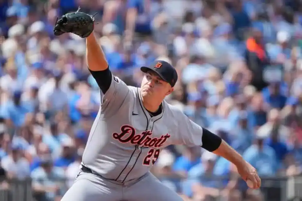 1 A baseball pitcher in a gray Detroit Tigers uniform winds up to throw against a blurred crowd in the background during a sunny game.