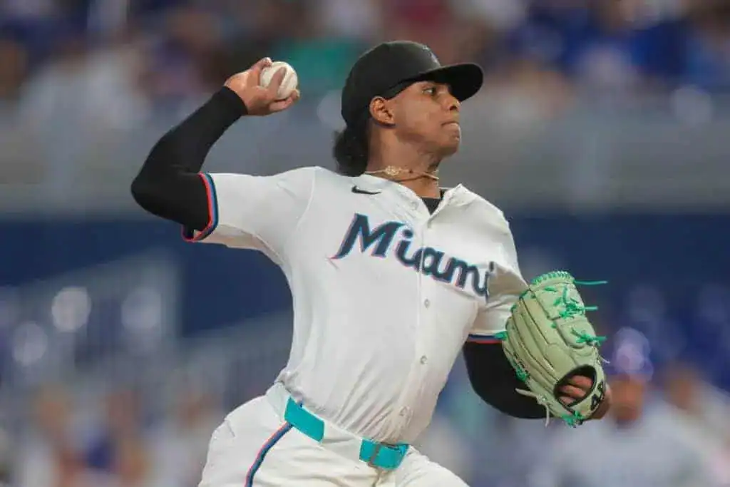 A Miami baseball player in a white jersey winds up to pitch, wearing a glove and black cap,
