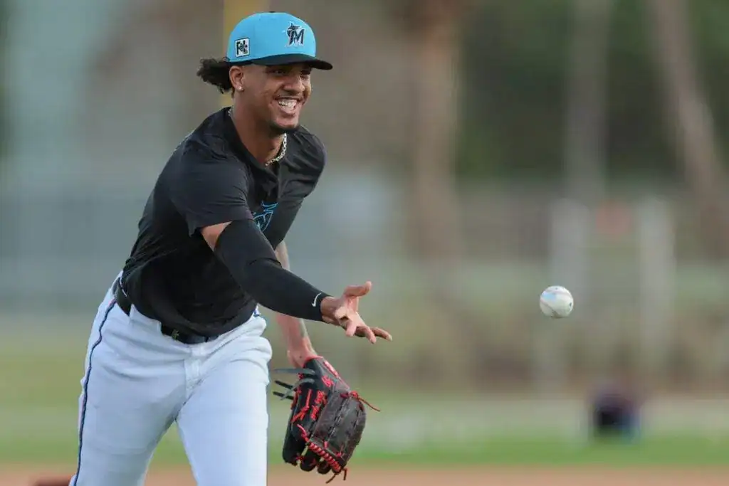 5 A player wearing a black shirt and white pants prepares to catch a baseball during practice, with palm trees in the background.