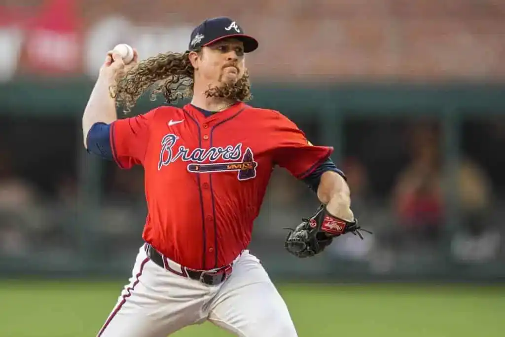 A baseball player in a red Braves jersey winds up to pitch, showcasing his iconic curly hair and athletic stance on the field.