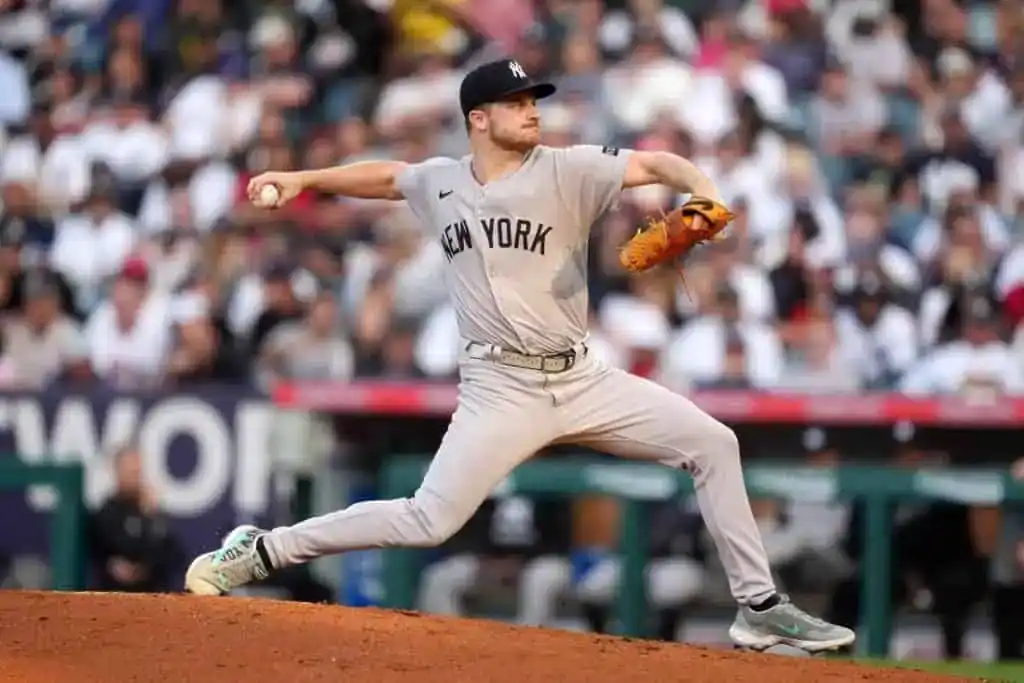 A baseball pitcher in a gray New York Yankees uniform winds up to throw a pitch on a field crowded with fans in the background.