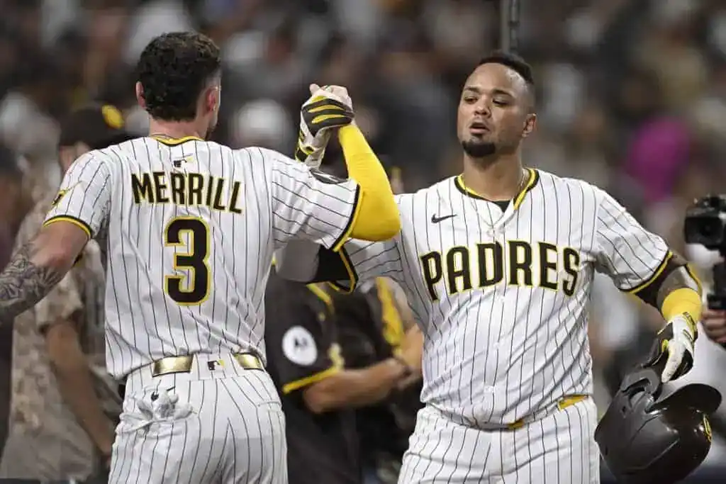 Two baseball players in white pinstriped uniforms celebrate a victory, with one patting the other's back and smiling.