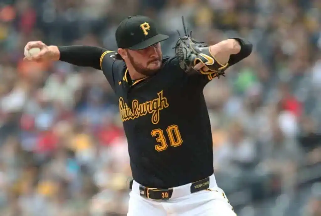 5 A pitcher in a black Pittsburgh Pirates jersey prepares to throw a baseball during a game, with fans blurred in the background.