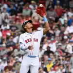 A Boston Red Sox player in a white uniform leaps to catch a baseball, with a packed crowd cheering in the background.