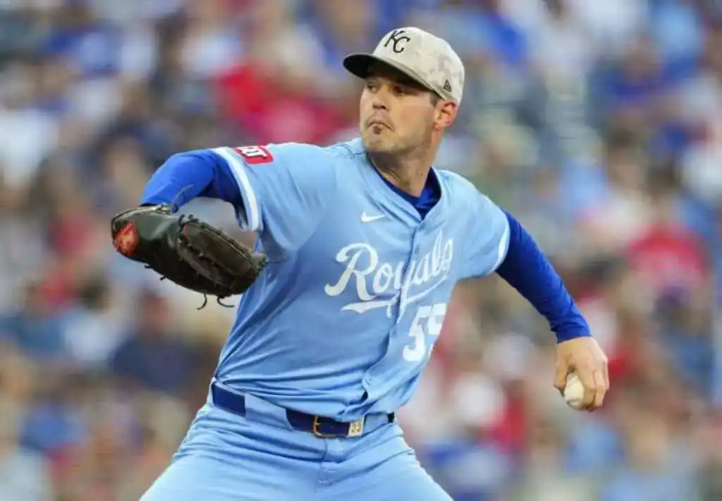 A baseball player in a light blue uniform is preparing to pitch, showcasing a focused expression and a vigorous throwing motion.