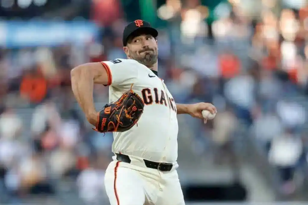 A pitcher from the San Francisco Giants throws a baseball on the field, wearing a white uniform with orange accents.