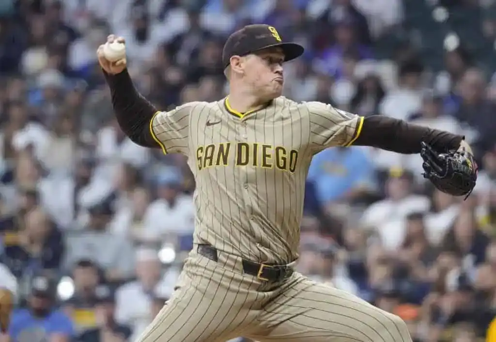 2 A San Diego Padres pitcher winds up to throw a baseball, wearing a tan and brown striped uniform, with a crowded stadium in background.