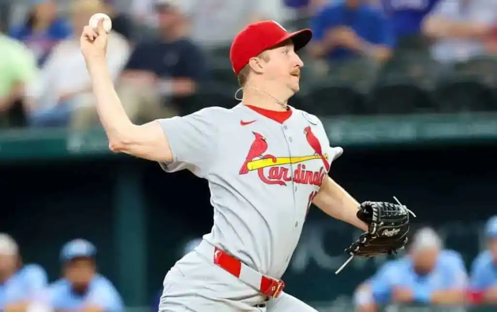 4 A pitcher in a gray St. Louis Cardinals uniform is winding up to throw a baseball during a game, with spectators in the background.