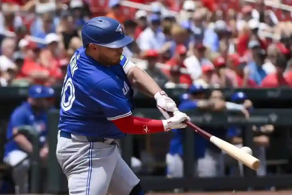 1 A baseball player in a blue jersey swings a bat during a game, surrounded by a cheering crowd in red and blue attire.