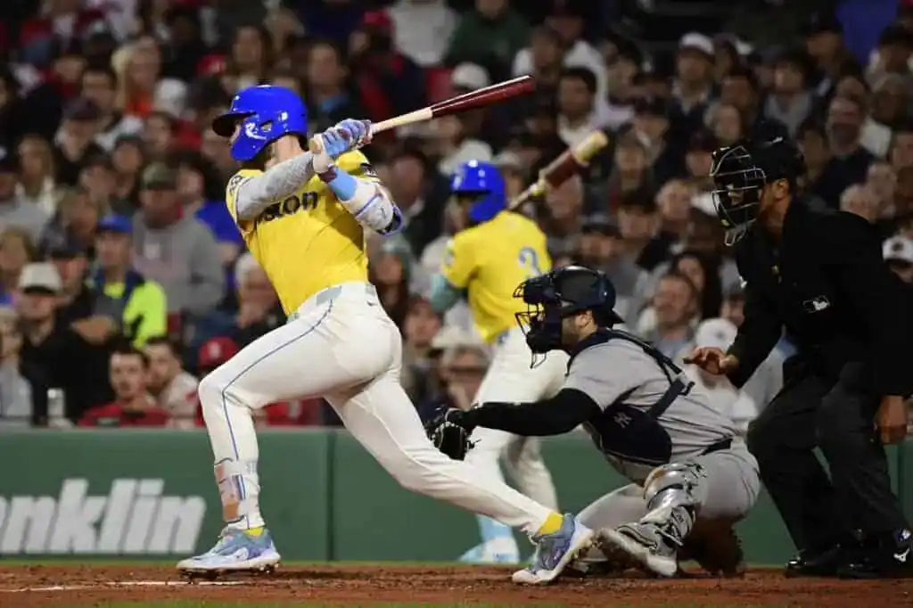 A baseball player swings a bat during a game, with a catcher crouching behind home plate and an umpire observing nearby.