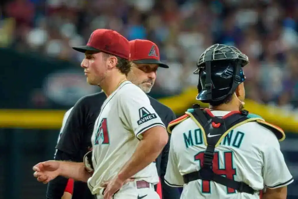 Two baseball players in the Arizona Diamondbacks uniform converse on the field during a game, with one in catcher gear.